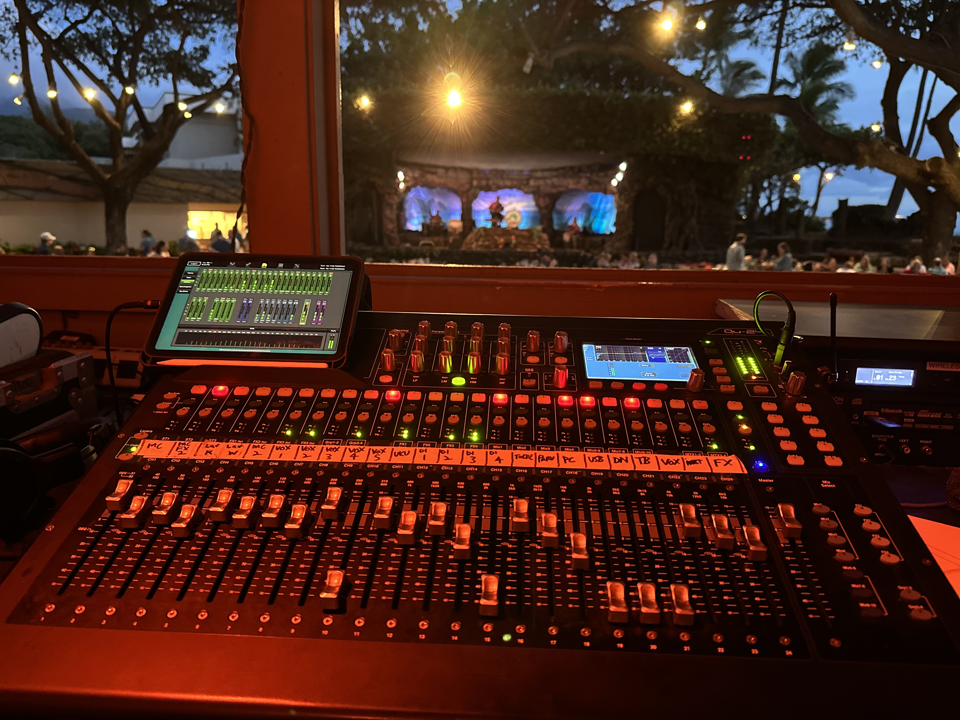 Front view of a large digital mixing console with illuminated controls at a live event