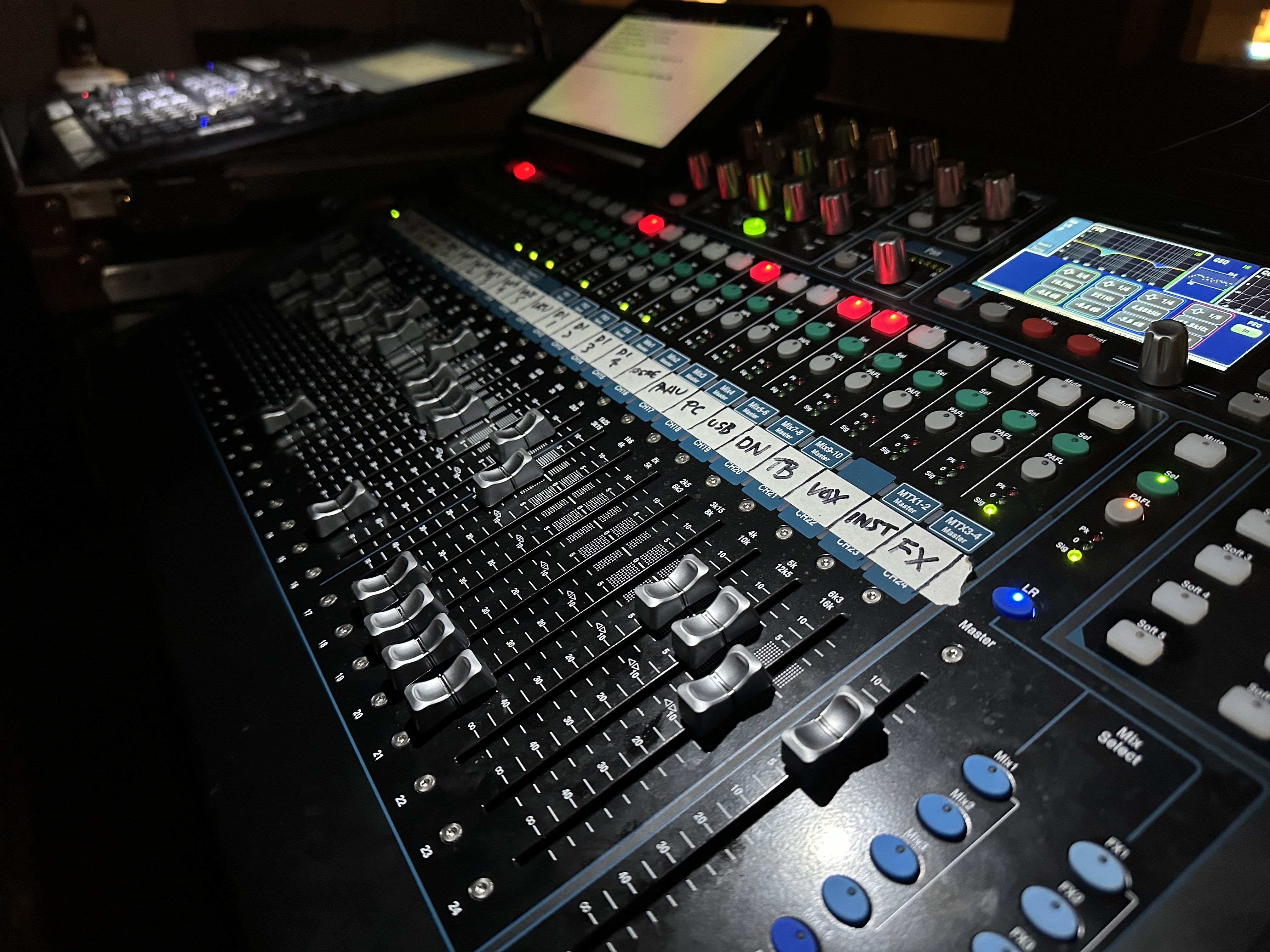 Side view of a digital mixing console lit up during a live event in a busy production area